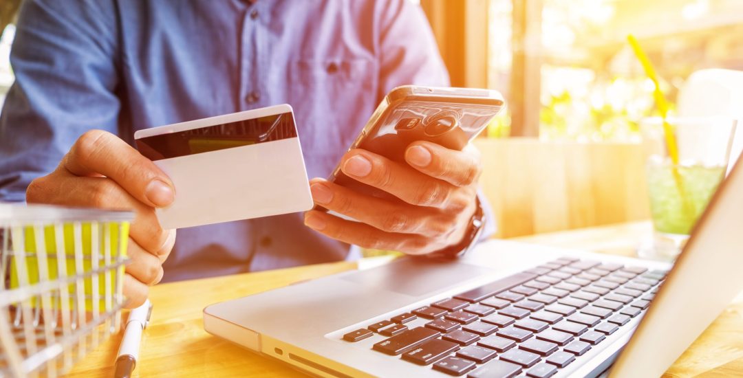 Man holding credit card in hand and entering security code using laptop keyboard.