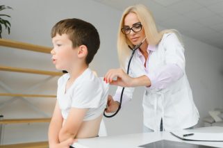 Pediatrician listening to breathing in the lungs and heartbeat with stethoscope. Portrait of adorable little boy visiting doctor