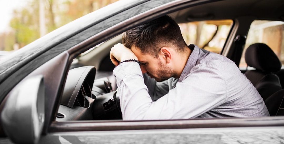 Young man sitting in his car very upset and stressed after hard failure and moving in traffic jam