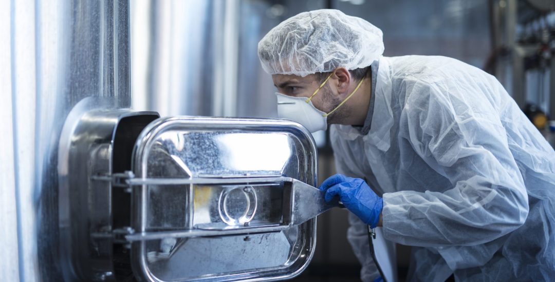 Technologist industrial worker in hazardous suit handling aggressive materials in chemical industry.