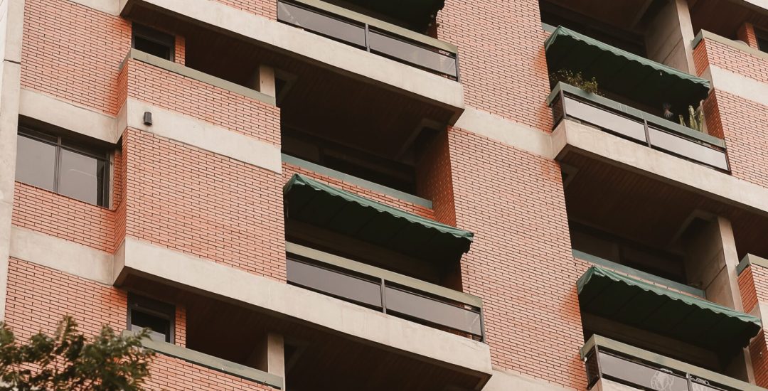 A low angle shot of a tall apartment building with greenery below