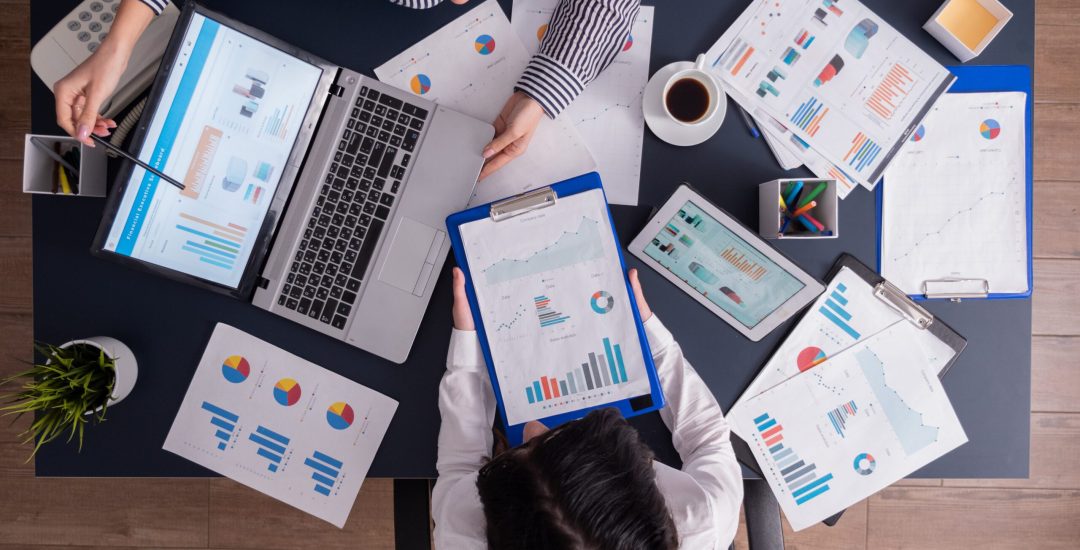 Top viewTop view of manager and employee doing teamwork in business office , looking at charts on laptop display. Finance paperwork with charts at workplace. Discusing financial plan.