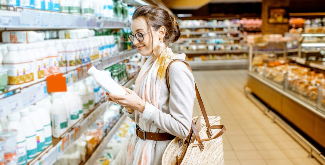 Young woman choosing milk standing near the shelves with dairy products in the supermarket