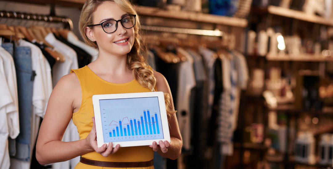 young-caucasian-woman-standing-in-boutique-shop-and-showing-tablet-with-business-graph