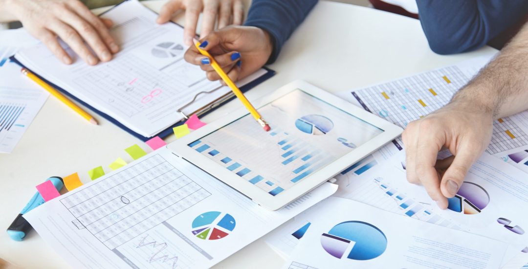 Cropped shot of people of diverse races working on business plan, analyzing value of goods, services, growth rate, making review of market situation, counting loss, using modern devices and touch pad